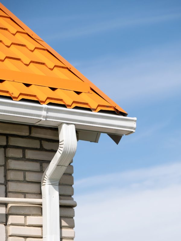 Rain Gutter Pipeline System on brick house , bright orange metal tile roof against blue sky